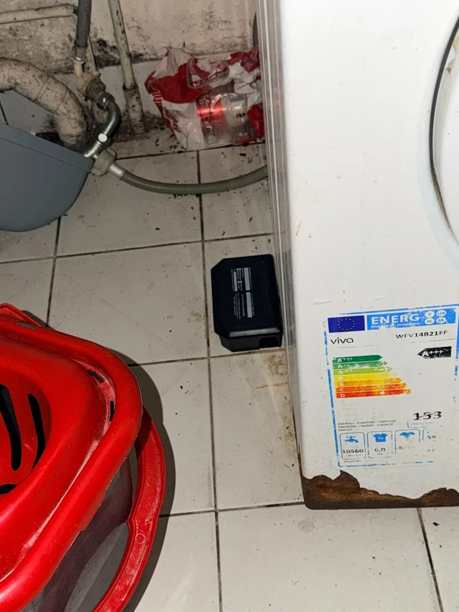 Poste de dératisation au sol à côté d’un lave-linge et de tuyaux